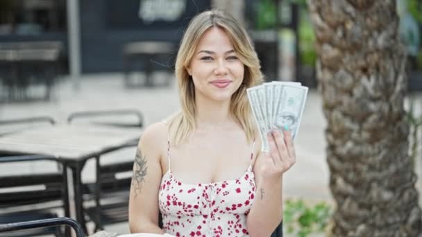 年轻的金发女人指着坐在咖啡店阳台上的美元 — 图库视频影像
