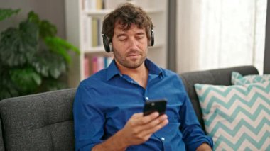 Genç İspanyol adam evdeki kanepede rahat bir şekilde müzik dinliyor.