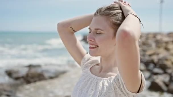 在海滩上 年轻的金发女游客带着自信的微笑抚摸着头发 — 图库视频影像