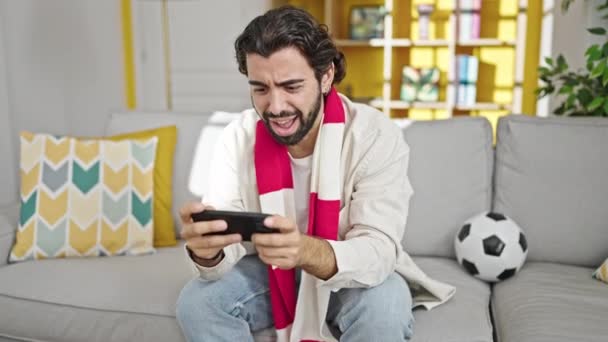 自宅で祝うソファーに座ってサッカーの試合を見ている若いヒスパニックの男 — ストック動画