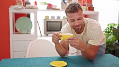 Genç adam yemek odasındaki masaya yaslanmış kahve içiyor.