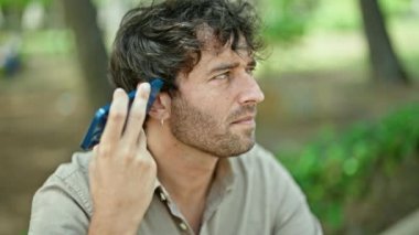 Genç İspanyol adam parkta bankta oturmuş sesli mesaj dinliyor.