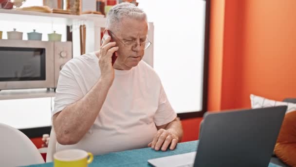 Μεσήλικας Γκριζομάλλης Μιλάει Στο Smartphone Χρησιμοποιώντας Laptop Στην Τραπεζαρία — Αρχείο Βίντεο