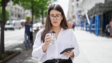 Akıllı telefon kullanan genç, güzel İspanyol kadın Madrid sokaklarında kahve içiyor.