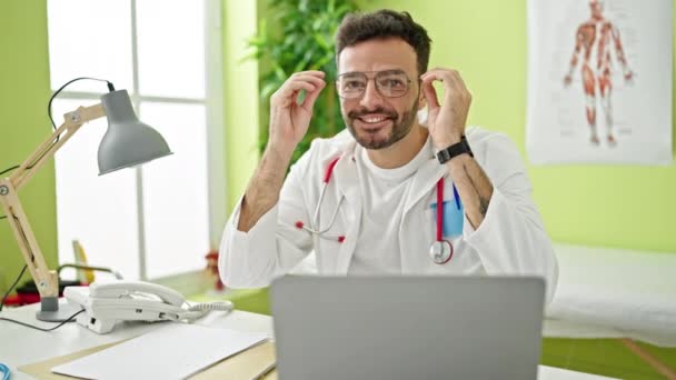 Молодий Іспаномовний Лікар Допомогою Ноутбука Знімає Окуляри Посміхаючись Клініці — стокове відео