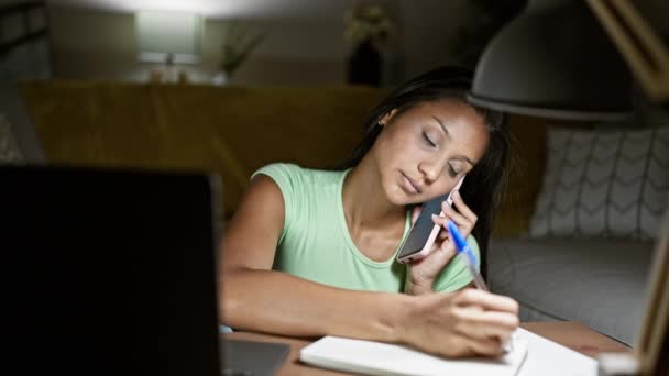 年轻的拉丁女人在家里用笔记本电脑记笔记 用智能手机聊天 — 图库视频影像