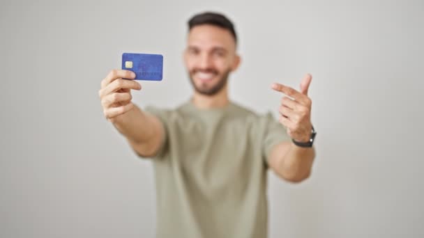 単離された白い背景の上に笑顔で親指を上げるクレジットカードを持っている若いヒスパニックの男 — ストック動画