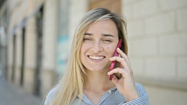 Genç sarışın kadın gülümsüyor. Kendine güveni tam. Akıllı telefondan konuşuyor.