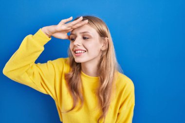 Mavi arka planda dikilen beyaz bir kadın çok mutlu ve gülümsüyor. arama kavramı. 