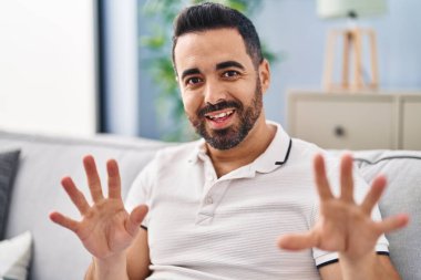 Young hispanic man sitting on sofa talking at home