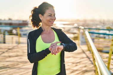 Middle age hispanic woman working out with smart watch at promenade