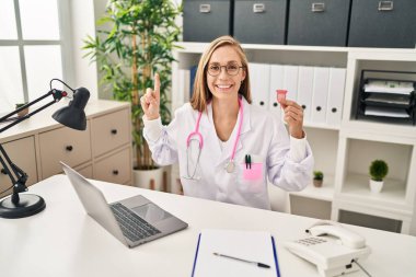 Genç sarışın doktor, elinde regl fincanı ile mutlu bir şekilde gülümsüyor. 