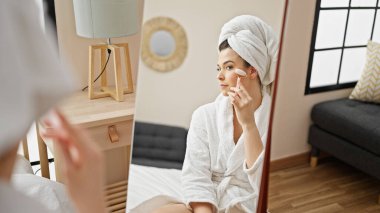 Genç, güzel, İspanyol bir kadın. Bornoz giyiyor. Yüzüne masaj yapıyor.