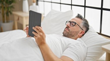 Yatak odasında dokunmatik ped kullanan gri saçlı bir adam.