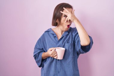 Orta yaşlı İspanyol kadın bir fincan kahve içiyor. Şoka girip yüzünü ve gözlerini kapatıyor. Utanmış bir ifadeyle parmaklarından bakıyor.. 