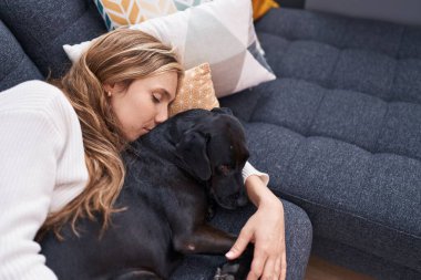 Young blonde woman lying on sofa sleeping with dog at home