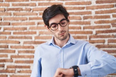 Tuğla duvar arkasında duran İspanyol genç adam kol saatindeki saati kontrol ediyor, rahat ve kendinden emin. 