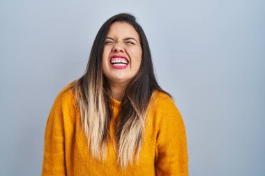 Young hispanic woman standing over isolated background angry and mad screaming frustrated and furious, shouting with anger. rage and aggressive concept. 