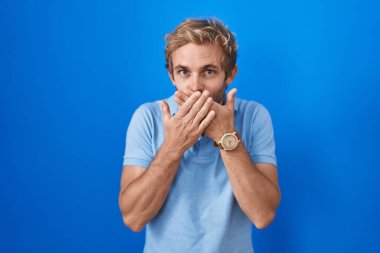 Mavi arka planda dikilen beyaz adam yanlışlıkla elleri ile ağzını kapatırken şok oldu. gizli kavram. 