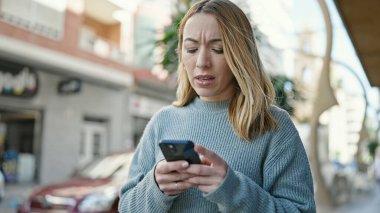 Sokakta akıllı telefon kullanan genç sarışın kadın.