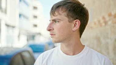 Sokakta ciddi bir ifadeyle yan tarafa bakan beyaz bir genç.