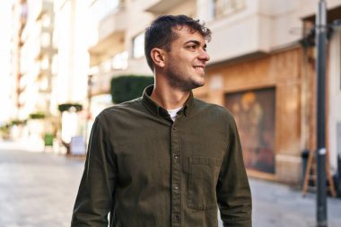 Young hispanic man smiling confident looking to the side at street