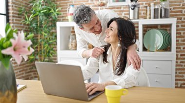 Üst düzey erkek ve kadın çift yemek odasında laptoplarını kullanıp kahve içiyorlar.