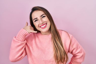 Pembe arka planda durup gülümseyen, el ve parmaklarıyla telefonla konuşan İspanyol bir kadın. iletişim kavramları. 