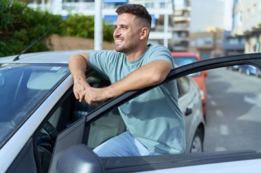 Genç İspanyol adam gülümsüyor. Sokakta araba kapısını açıyor.