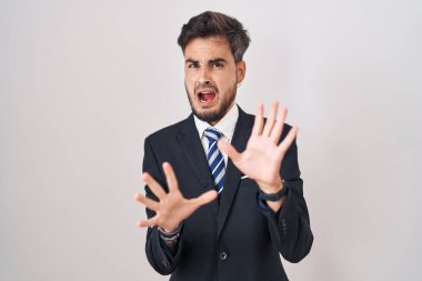 Dövmeli, takım elbiseli, kravatlı, korku ifadesinden dehşete düşmüş genç İspanyol adam. El hareketlerini bırak, şok içinde bağır. panik konsepti. 