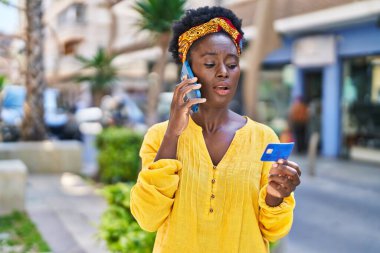 Genç Afrikalı Amerikalı kadın akıllı telefonla konuşuyor ve sokakta kredi kartı kullanıyor.