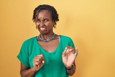 Sarı arka plan üzerinde duran Afrikalı kadın tiksindirici ve tiksindirici bir yüz ifadesi, tiksindirici bir yüz ifadesi.. 