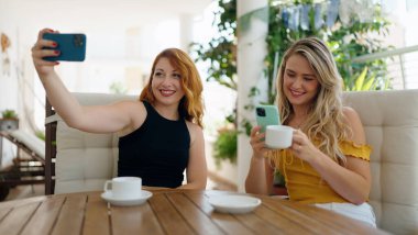 Evdeki terasta oturan iki kadın akıllı telefondan selfie çekiyor.