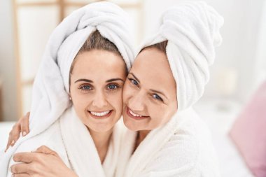 Two women mother and daughter wearing bathrobe hugging each other at bedroom