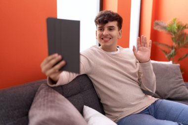 Kanepede oturan dokunmatik dokunmatik olmayan genç adam pozitif ve mutlu görünüyor ve kendine güvenen bir gülümsemeyle dişlerini gösteriyor. 