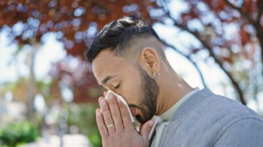 Parkta hapşıran polen alerjisi olan genç İspanyol adam.