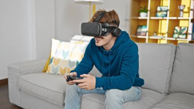 Evde video oyunu oynayan İspanyol genç adam joystick ve sanal gerçeklik gözlüğü kullanıyor.