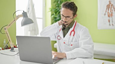 Genç İspanyol doktor klinikte rahim ağrısı çeken dizüstü bilgisayar kullanıyor.