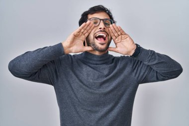 Handsome latin man standing over isolated background smiling cheerful playing peek a boo with hands showing face. surprised and exited 