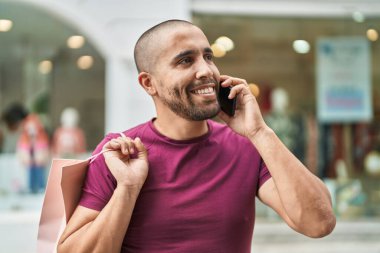 Genç latin adam akıllı telefondan konuşuyor. Elinde alışveriş çantası var.