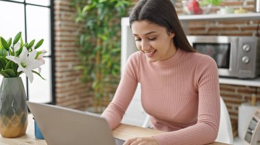 Yemek odasındaki masada dizüstü bilgisayar kullanan güzel İspanyol kadın.