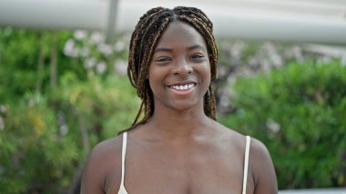 Afro-Amerikalı kadın parkta kendinden emin bir şekilde gülümsüyor.