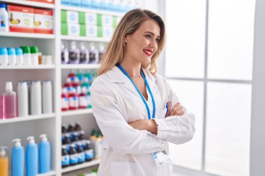 Young beautiful hispanic woman pharmacist smiling confident standing with arms crossed gesture at pharmacy