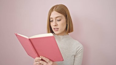 Soyutlanmış pembe arka planda kitap okuyan genç sarışın kadın.