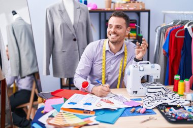 Genç İspanyol terzi gülümsüyor. Terzi dükkanında deftere kendine güvenen bir yazı yazıyor.