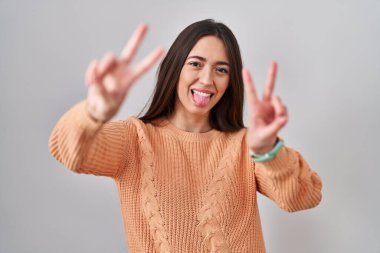 Genç esmer kadın beyaz arka planda duruyor. İki elini de göstererek gülümsüyor ve zafer işareti yapıyor. İki numara.. 