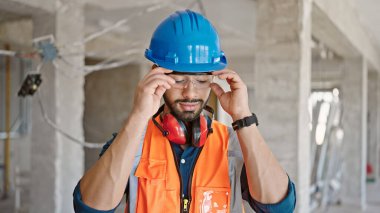 İnşaat alanında baret takan genç İspanyol müteahhit gözlüklerini çıkarıyor.