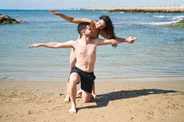 Young hispanic couple tourists wearing swimsuit standing with arms open at seaside