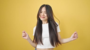 Genç Çinli kadın gülümsüyor, kendinden emin, izole edilmiş sarı arka planda dans ediyor.