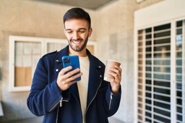 Genç İspanyol adam akıllı telefon kullanıyor, sokakta kahve içiyor.